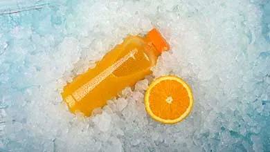 Close up one plastic PET bottle of fresh orange juice and cut half orange slice over background of crushed ice, elevated high angle view, directly above
